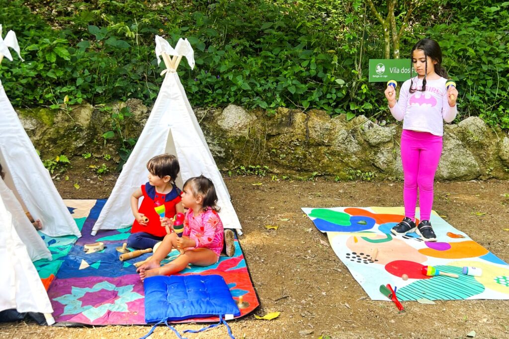 Crianças brincando em um espaço ao ar livre cercado pela natureza, com tendas infantis e atividades lúdicas durante uma festa infantil.