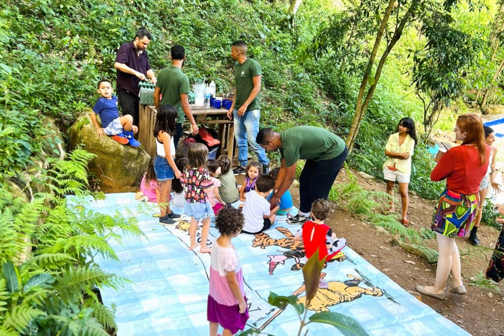 Crianças participando de atividades ao ar livre em meio à natureza durante uma festa infantil em espaço cercado por árvores e áreas verdes.